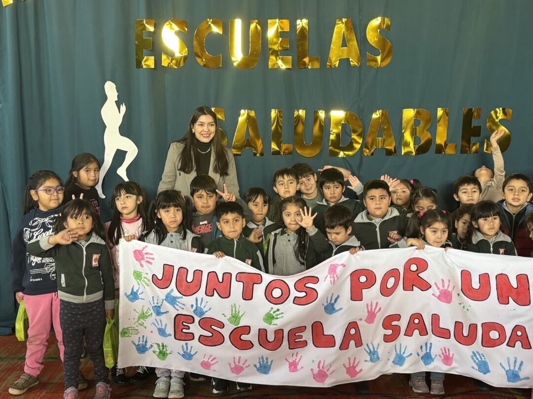 Estudiantes junto a su educadora sosteniendo el lienzo "Juntos por una escuela saludable" en el gimnasio